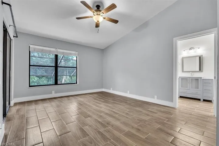 Spacious room featuring wood-finish tile flooring, vaulted ceilings, and a ceiling fan with integrated lighting