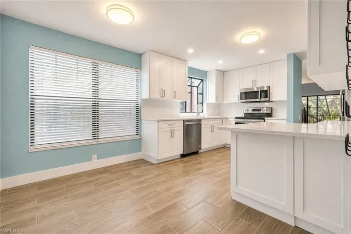 Modern kitchen featuring wood-finish flooring, white cabinetry, integrated stainless steel appliances, a white subway tile backsplash, and light-toned countertops