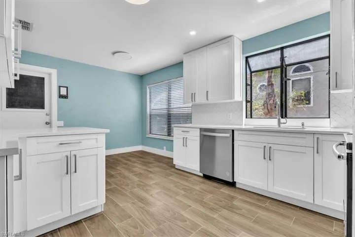 Modern kitchen featuring white shaker cabinetry, light-toned countertops, a stainless steel dishwasher, and wood-finish flooring