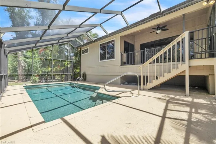 Screened-in swimming pool with an integrated spa, featuring a broad deck and direct access to an elevated balcony