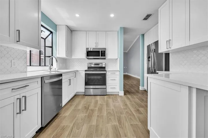 Contemporary kitchen featuring white shaker cabinetry, stainless steel appliances, white countertops, a decorative scalloped tile backsplash, and wood-finish flooring