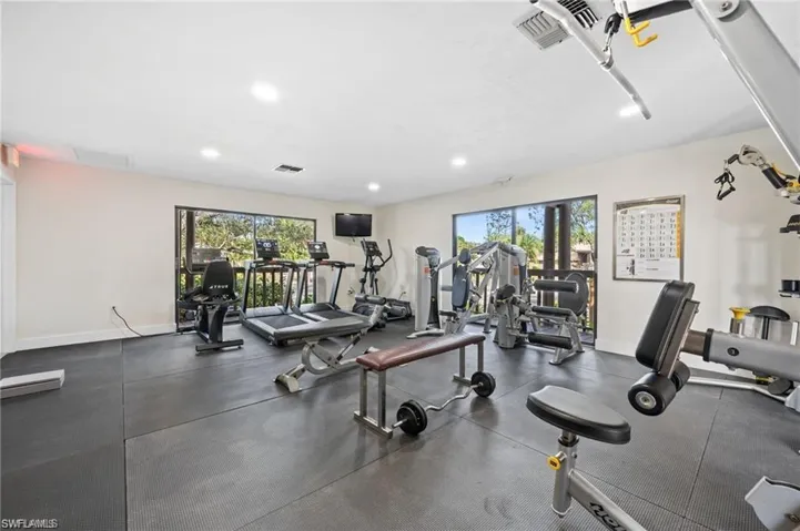 Expansive fitness room featuring resilient rubber flooring, large windows, recessed ceiling lighting, and a wall-mounted display