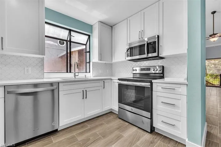 Updated kitchen featuring white shaker cabinetry, stainless steel appliances, a white scallop-patterned tile backsplash, white countertops, and wood-finish tile flooring