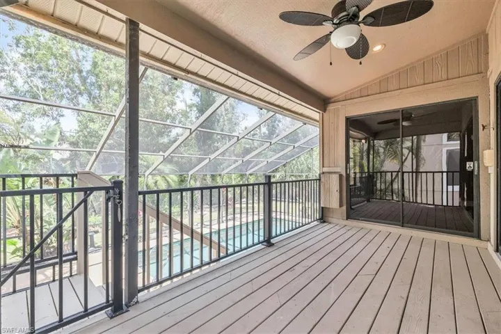Screened-in outdoor patio featuring wood-finish decking, black metal railings, a ceiling fan, and sliding glass doors