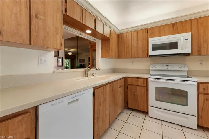 Kitchen with white appliances, light countertops, light tile patterned flooring, and wood finish cabinetry