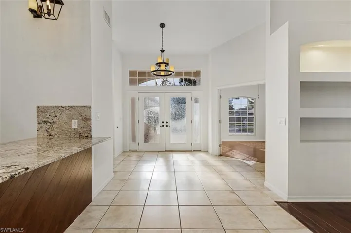 Tiled foyer entrance featuring an inviting chandelier, french doors, and a high ceiling