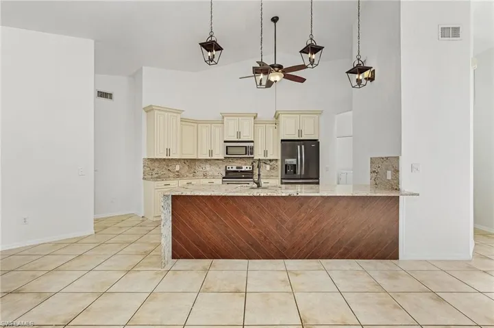 Kitchen with ceiling fan, cream cabinetry, decorative backsplash, high vaulted ceiling, and appliances with stainless steel finishes