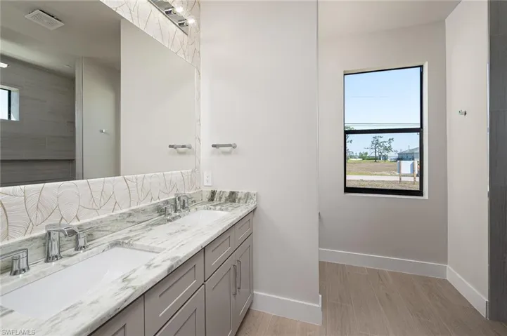 Full bathroom featuring double vanity, light wood-style floors, and tasteful backsplash