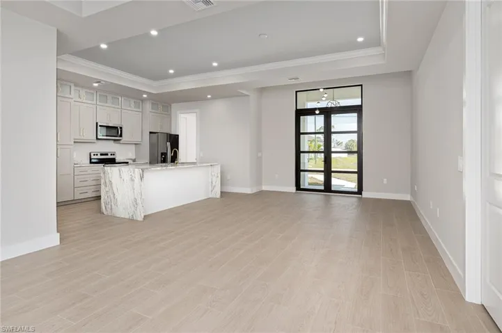Kitchen with glass insert cabinets, an island with sink, light stone counters, open floor plan, and appliances with stainless steel finishes