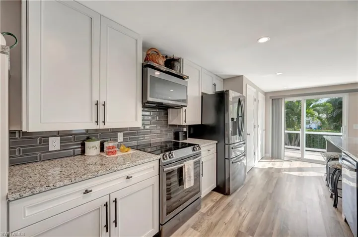 Kitchen featuring light stone countertops, tasteful backsplash, stainless steel appliances, white cabinets, and light hardwood / wood-style floors