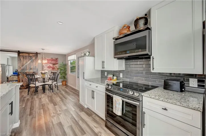Kitchen with light stone countertops, a barn door, decorative light fixtures, white cabinets, and appliances with stainless steel finishes