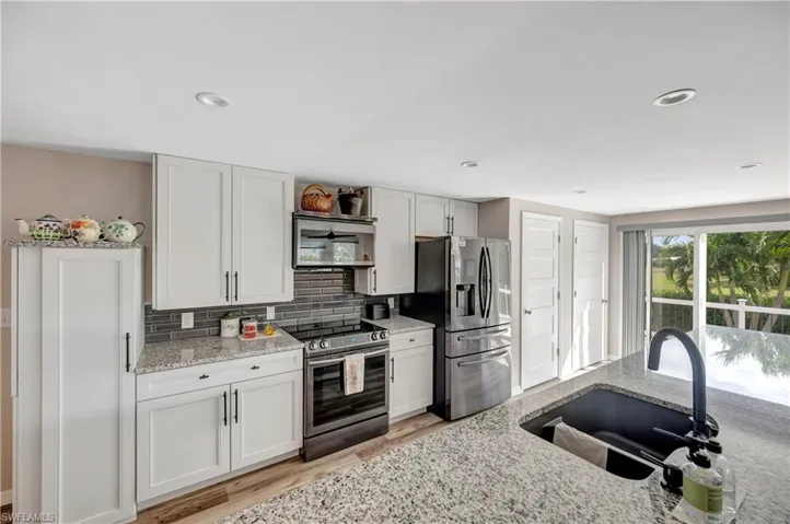 Kitchen featuring decorative backsplash, light stone countertops, stainless steel appliances, sink, and white cabinets