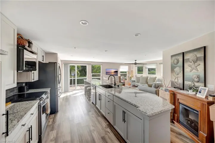 Kitchen featuring white cabinetry, sink, light stone counters, a center island with sink, and appliances with stainless steel finishes