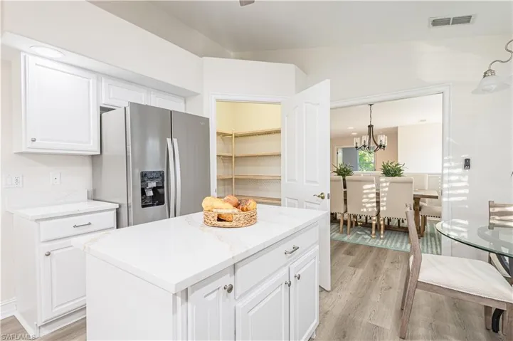 Kitchen with stainless steel refrigerator with ice dispenser, white cabinets, a center island, and light wood-style floors