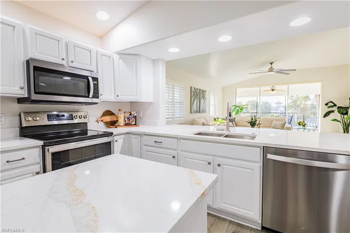 Kitchen featuring light stone counters, stainless steel appliances, white cabinetry, lofted ceiling, and open floor plan
