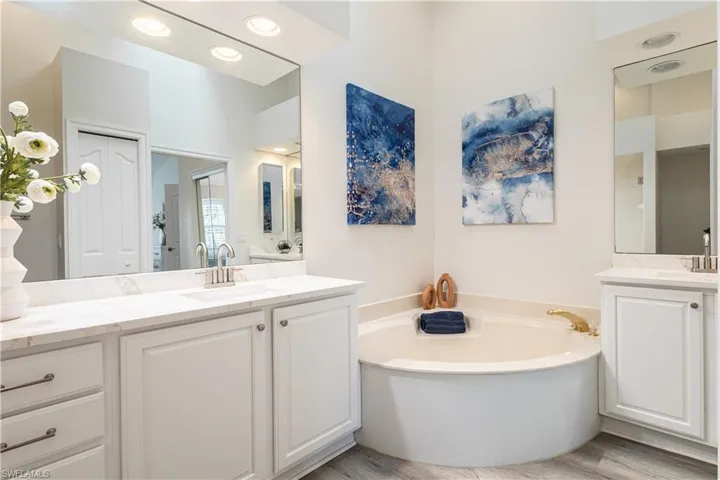 Bathroom featuring two vanities, light wood-type flooring, a bath, and recessed lighting