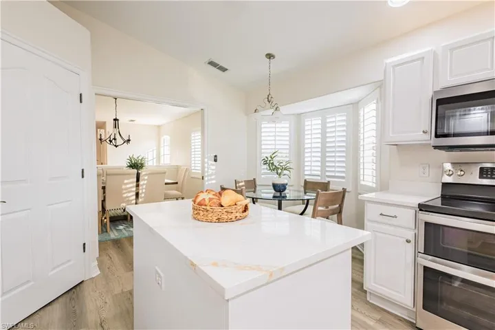 Kitchen with stainless steel appliances, vaulted ceiling, light wood-type flooring, white cabinets, and a chandelier
