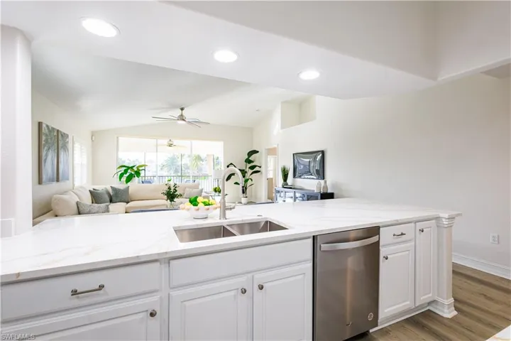 Kitchen with open floor plan, stainless steel dishwasher, light stone countertops, white cabinetry, and light wood-style flooring