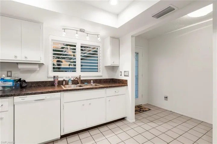 Kitchen with dishwasher, dark countertops, white cabinets, light tile patterned floors, and recessed lighting