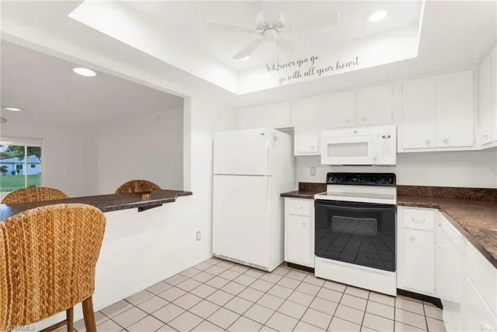 Kitchen featuring white appliances, dark countertops, a tray ceiling, recessed lighting, and white cabinetry