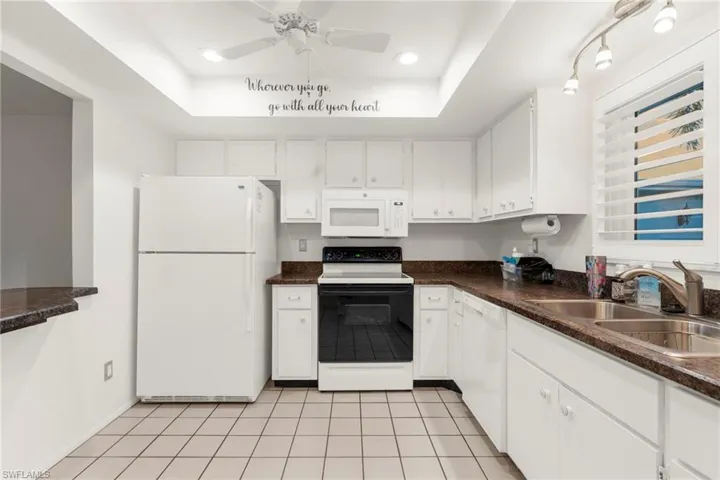 Kitchen with white appliances, white cabinetry, dark countertops, light tile patterned floors, and a tray ceiling