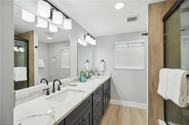 Full bath featuring light wood-type flooring, double vanity, recessed lighting, and a shower stall