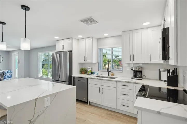 Kitchen with appliances with stainless steel finishes, light stone counters, light wood-type flooring, white cabinetry, and hanging light fixtures