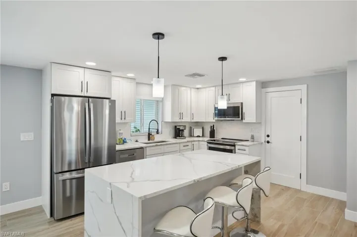 Kitchen with appliances with stainless steel finishes, white cabinetry, light stone counters, decorative light fixtures, and recessed lighting