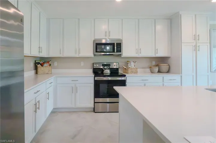 White cabinetry with silver-tone hardware, stainless steel appliances, light-toned countertops, and large format floor tiling