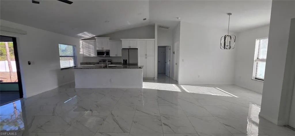 Kitchen with light marble finish floors, white cabinets, healthy amount of natural light, open floor plan, and a high ceiling