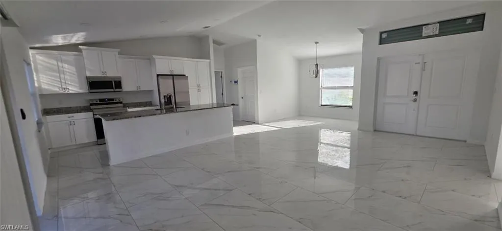 Kitchen featuring white cabinets, stainless steel appliances, dark stone countertops, a center island with sink, and decorative light fixtures