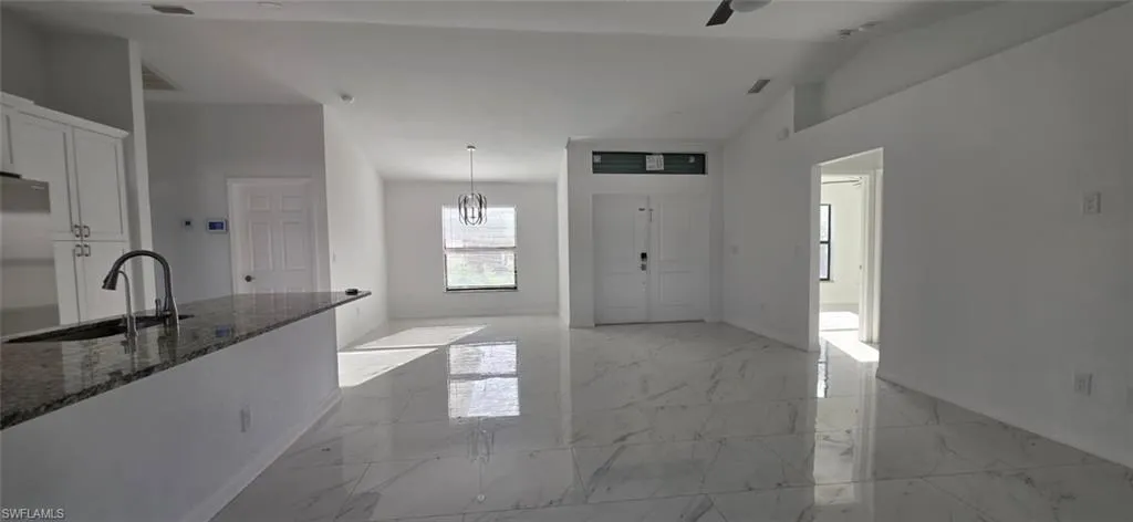 Kitchen featuring white cabinetry, light marble finish floors, dark stone counters, stainless steel refrigerator, and lofted ceiling