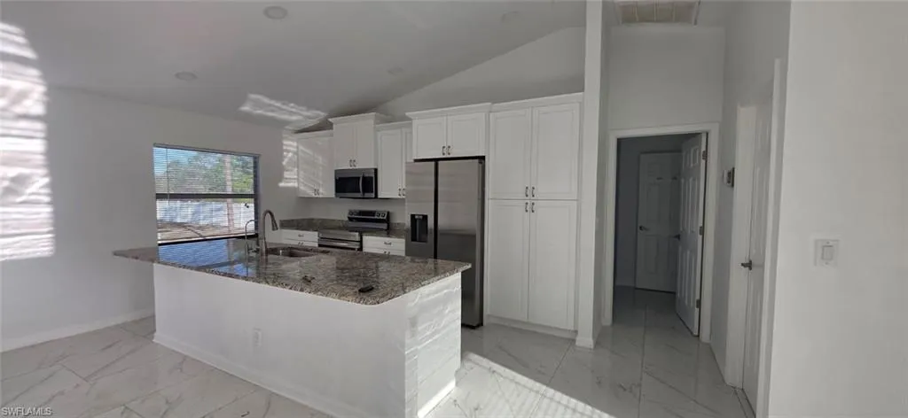 Kitchen with stainless steel appliances, dark stone counters, white cabinetry, lofted ceiling, and light marble finish floors