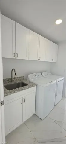 Laundry area featuring cabinet space, light marble finish floors, and separate washer and dryer