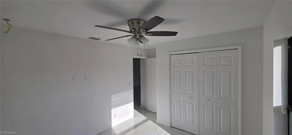 Unfurnished bedroom with light marble finish flooring, ceiling fan, and a closet