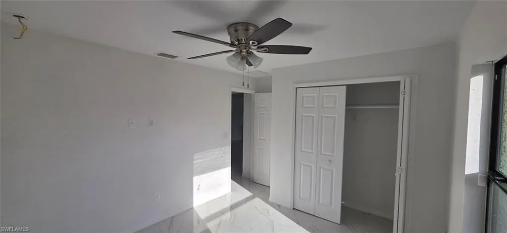 Unfurnished bedroom featuring a closet, light marble finish flooring, and a ceiling fan