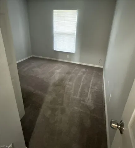 Spare room featuring dark carpet and baseboards