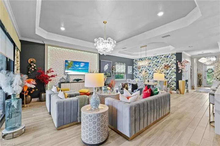 Living area with a chandelier, tile finish floors, crown molding, an accent wall, and a tray ceiling