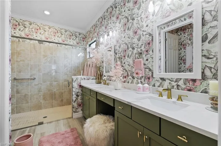 Full bathroom featuring double vanity, wallpapered walls, a stall shower, and crown molding