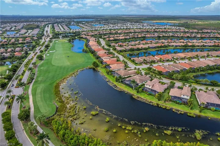Aerial view of property and surrounding area featuring nearby suburban area, a large body of water, and a golf course