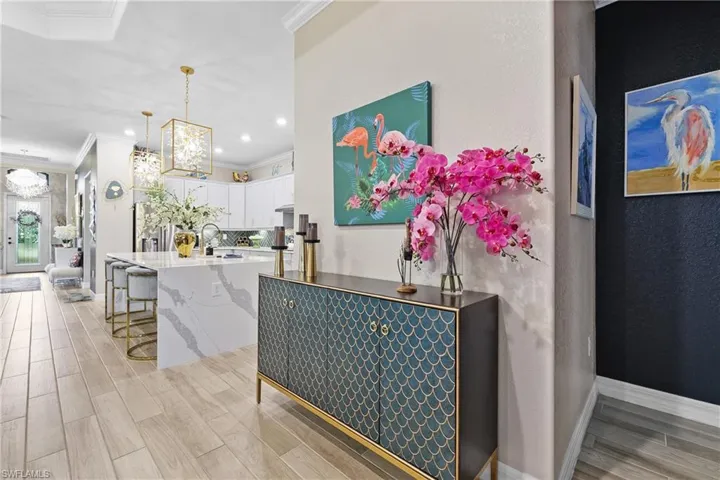 Kitchen with white cabinetry, tile finish floors, crown molding, hanging light fixtures, and light stone counters
