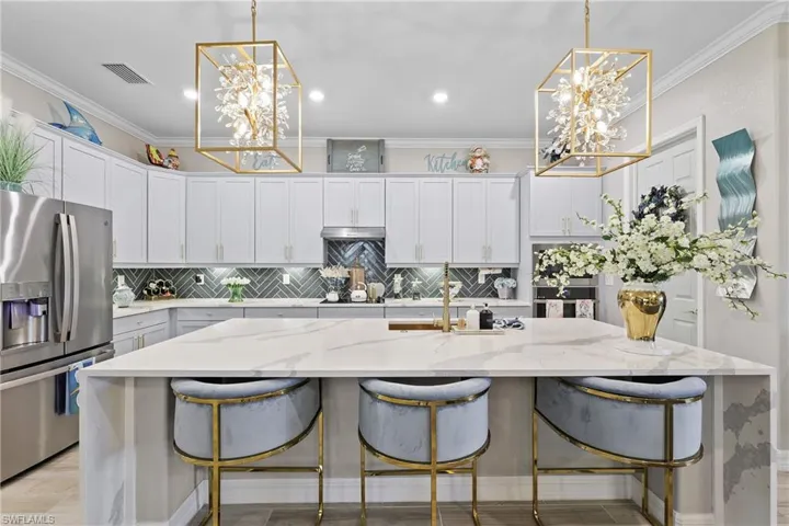 Kitchen with a chandelier, light stone counters, backsplash, stainless steel fridge with ice dispenser, and ornamental molding