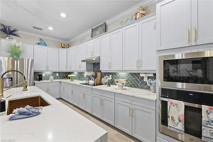 Kitchen featuring appliances with stainless steel finishes, light stone countertops, decorative backsplash, ornamental molding, and recessed lighting
