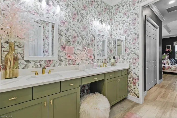 Full bathroom featuring double vanity, wallpapered walls, a stall shower, and crown molding