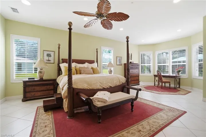 Spacious primary suite offers a private retreat with office nook/seating area, custom lighting, plantation shutters, and a beautifully finished bath with oversized shower, large tub, dual vanities, floor-to-ceiling tile and upgraded fixtures