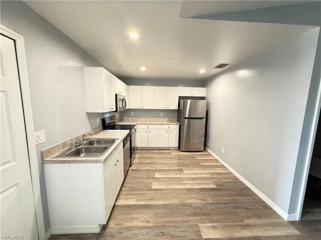 Kitchen with white cabinets, stainless steel appliances, light laminate floors, light countertops, and recessed lighting