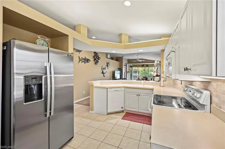 Kitchen with decorative backsplash, white cabinetry, appliances with stainless steel finishes, light tile patterned floors, and kitchen peninsula
