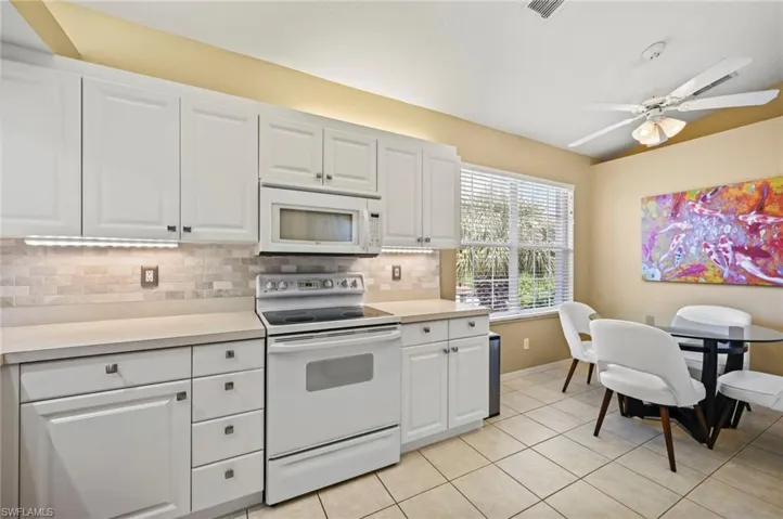 Kitchen with backsplash, white cabinetry, white appliances, ceiling fan, and light tile patterned flooring