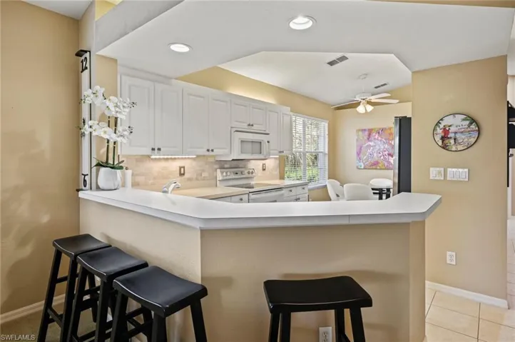 Kitchen featuring ceiling fan, decorative backsplash, light tile patterned floors, a breakfast bar area, and white appliances