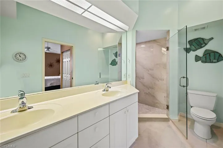 Bathroom featuring tile patterned flooring, ceiling fan, double vanity, toilet, and walk in shower